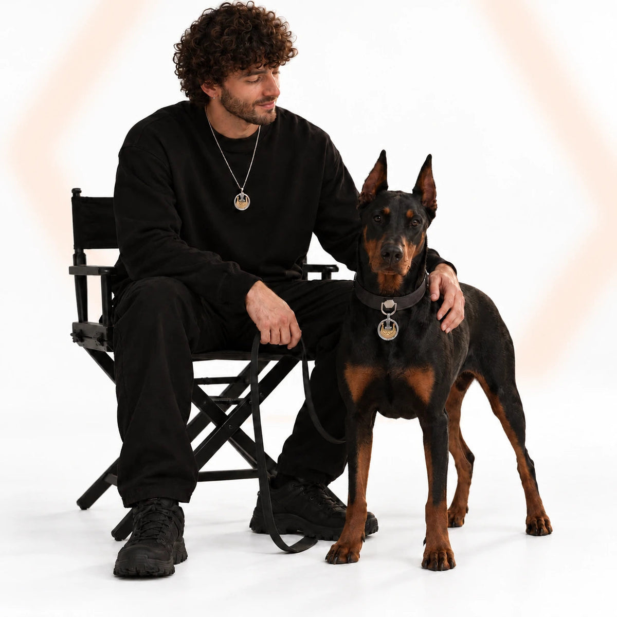 A man and Doberman wearing matching Valhalla accessories against a white backdrop with a softly blurred orange hexagon.