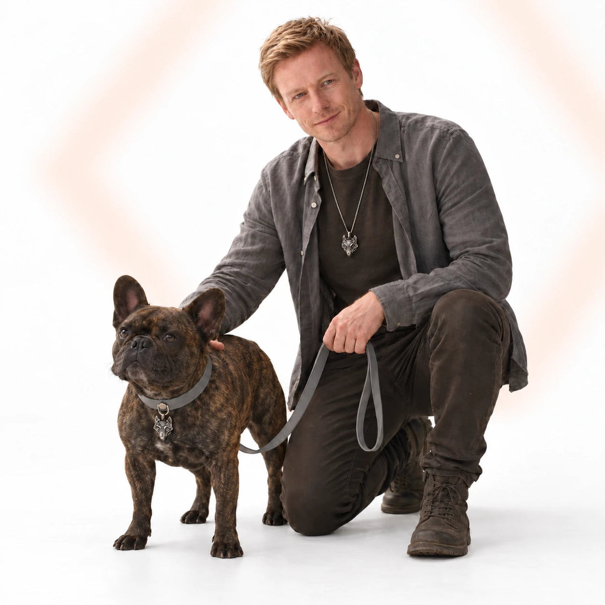 A man and French Bulldog wearing matching Wolf accessories with a grey collar against a soft white backdrop.